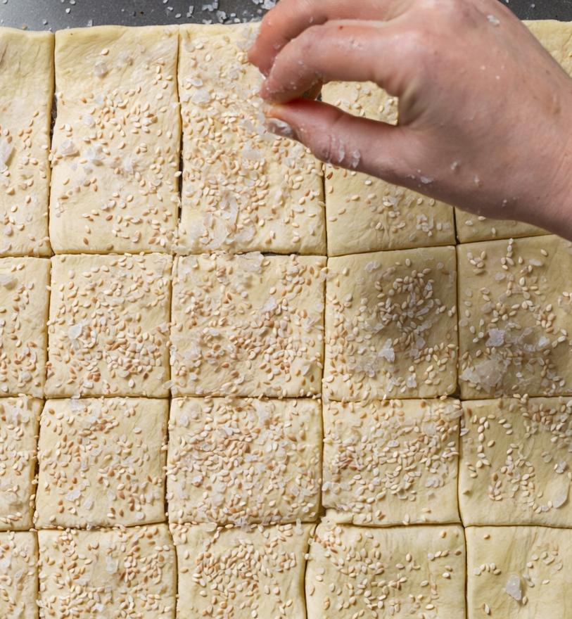 Sprinkling sesame seeds and flaky sea salt over sourdough discard crackers before baking.